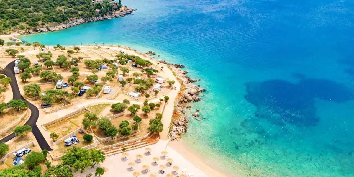 Campingplatz am Meer mit Olivenbäumen – Luftaufnahme Kroatien Luftaufnahme eines Campingplatzes mit Wohnmobilen und Olivenbäumen direkt am türkisblauen Meer, Sandstrand mit Sonnenschirmen im Vordergrund