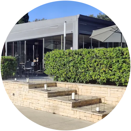 Terrasse des Restaurants Mol Picio im Bereich Colona des Campingplatzes Mon Perin mit moderner Glasfront und gepflegter Hecke