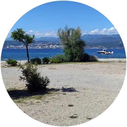 Panoramablick auf das Meer und Motorboot am Camping Omišalj Blick von einem kiesigen Stellplatz auf dem Campingplatz Omišalj über vereinzelte mediterrane Sträucher hinweg auf das blaue Meer, ein Motorboot und die gegenüberliegende Küste unter blauem Himmel.