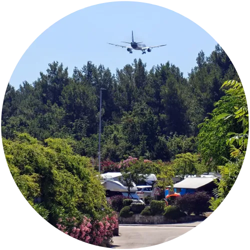 Flugzeug im Landeanflug über dem Campingplatz Omišalj auf Krk Ein Passagierflugzeug fliegt im tiefen Landeanflug über die dichten grünen Bäume und Stellplätze des Campingplatzes Omišalj bei blauem Himmel.