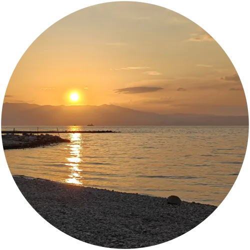 Malerischer Sonnenuntergang am Meer in Omišalj auf Krk Die goldene Abendsonne geht über dem Meer und den Bergen im Hintergrund unter, spiegelt sich im Wasser und beleuchtet den Kieselstrand von Omišalj.