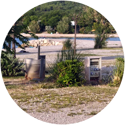 Strom-, Wasser- und Abwasseranschluss am Stellplatz des Camping Omišalj Eine moderne Stromsäule mit CEE-Anschlüssen sowie eine Zapfstelle für Frischwasser und Abwasser direkt an einem Stellplatz des Campingplatzes Omišalj mit Blick auf den Strandbereich.