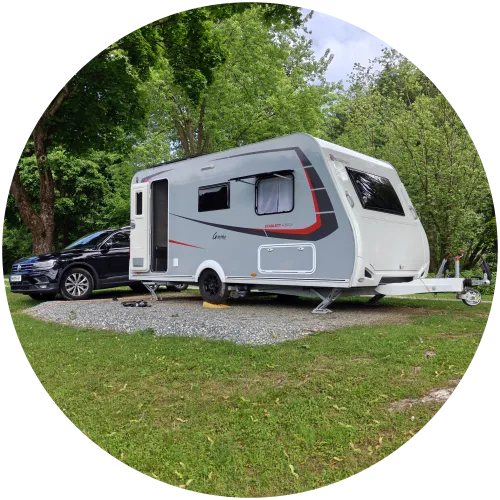 Wohnwagen Stellplatz auf dem Campingplatz am Sulmsee Ein moderner Sterckeman Wohnwagen mit Auto auf einem Schotter-Stellplatz auf dem Campingplatz Sulmsee, umgeben von grünen Bäumen und Wiese.