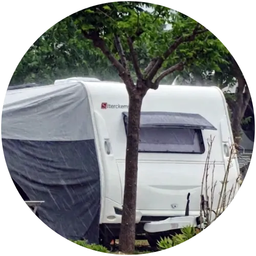 Wohnwagen Nahaufnahme im strömenden Regen auf Campingplatz Nahaufnahme eines weißen Wohnwagens mit Vorzelt bei starkem Regen unter grünem Baum auf Campingplatz